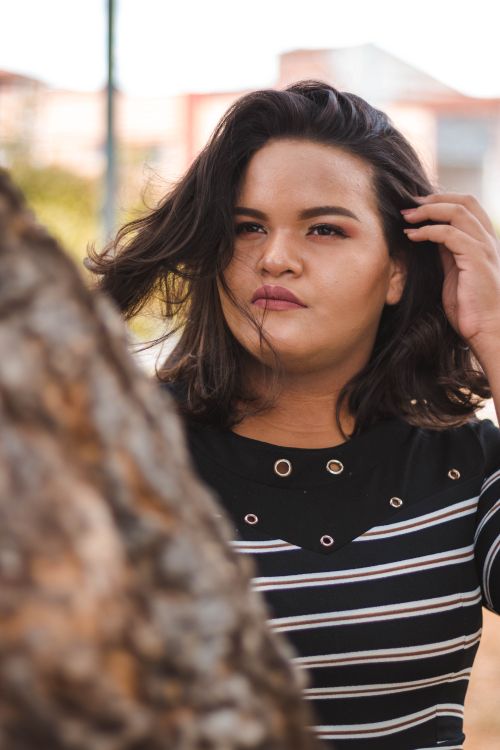 Free Close-up portrait of a woman touching her hair beside a tree. Stock Photo