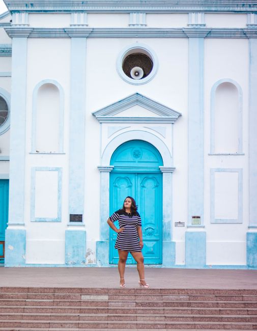 Plus-size woman in striped dress poses confidently on steps of a blue and white building.