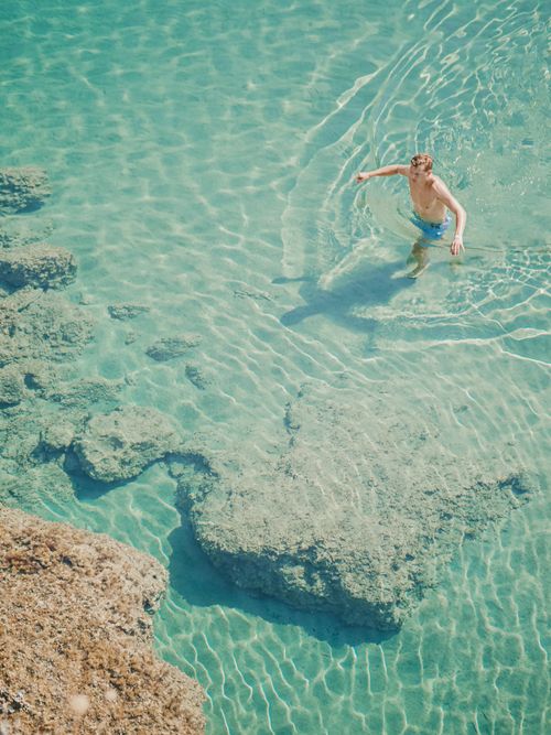 Free From above of unrecognizable male traveler with naked torso on rippled sea with transparent water Stock Photo