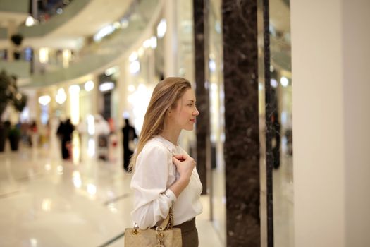 Side view of a stylish woman window shopping in a modern mall interior.