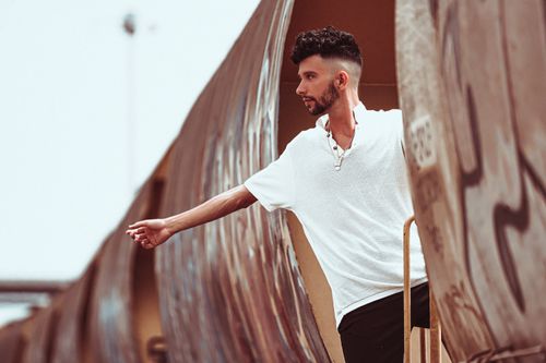 Free Stylish man in a white shirt posing on a train, with a modern urban backdrop. Stock Photo