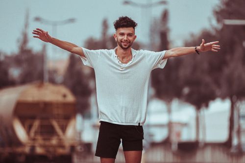 Free Portrait of a smiling young man in casual clothing posing outdoors with open arms. Stock Photo