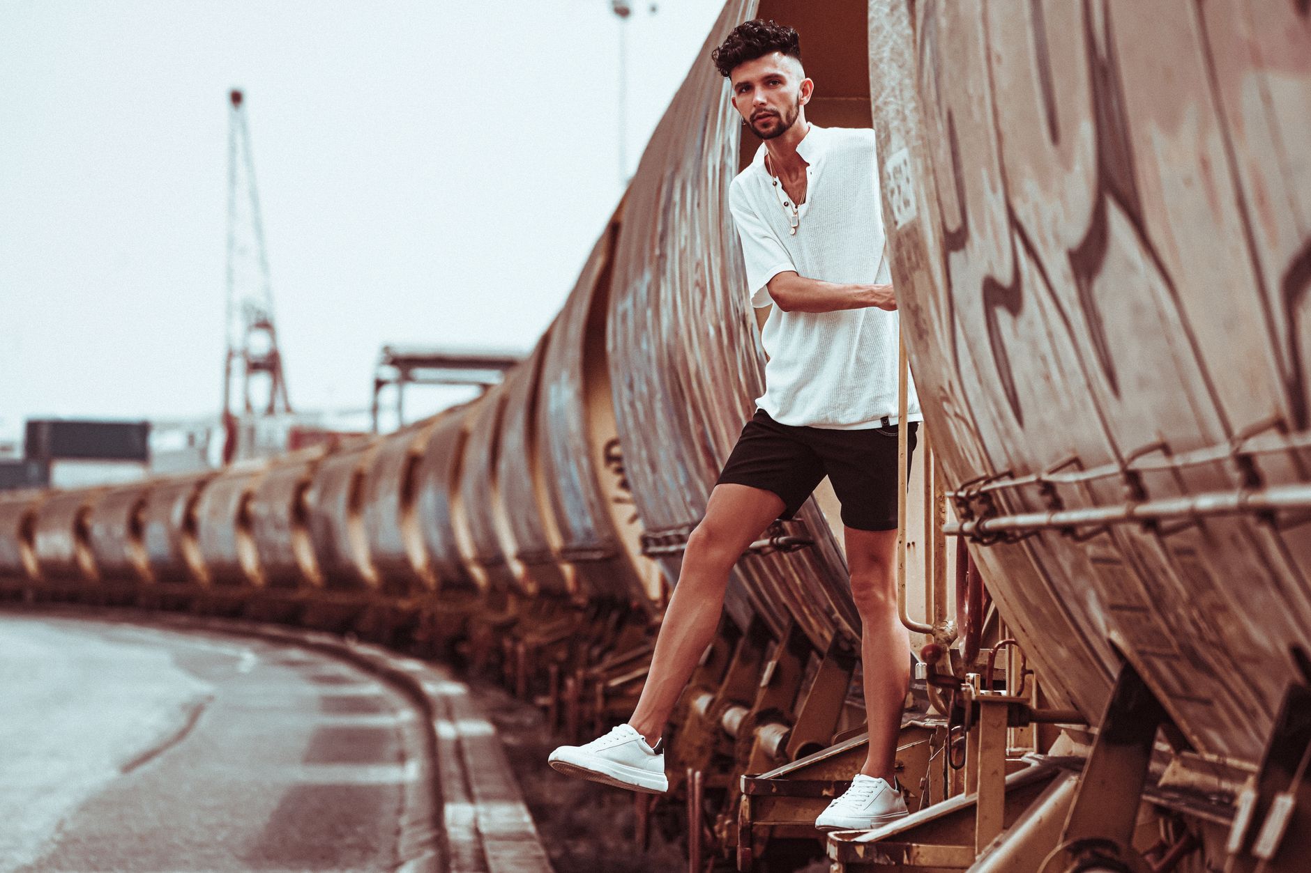 Homme en short noir et chemise blanche posant dans un décor urbain industriel