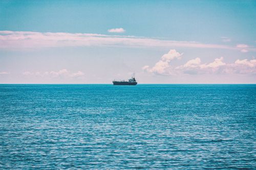 Free A cargo ship sails alone on a tranquil ocean under a bright sky. Stock Photo
