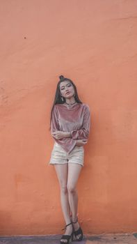 Young woman in fashionable attire posing against a bold orange backdrop for a stylish urban look.