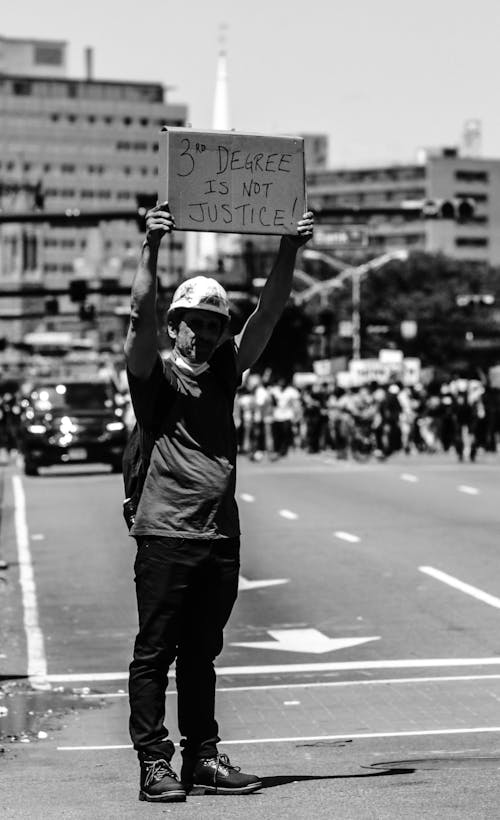 Black and white of male holding placard and standing on road against crowd of people