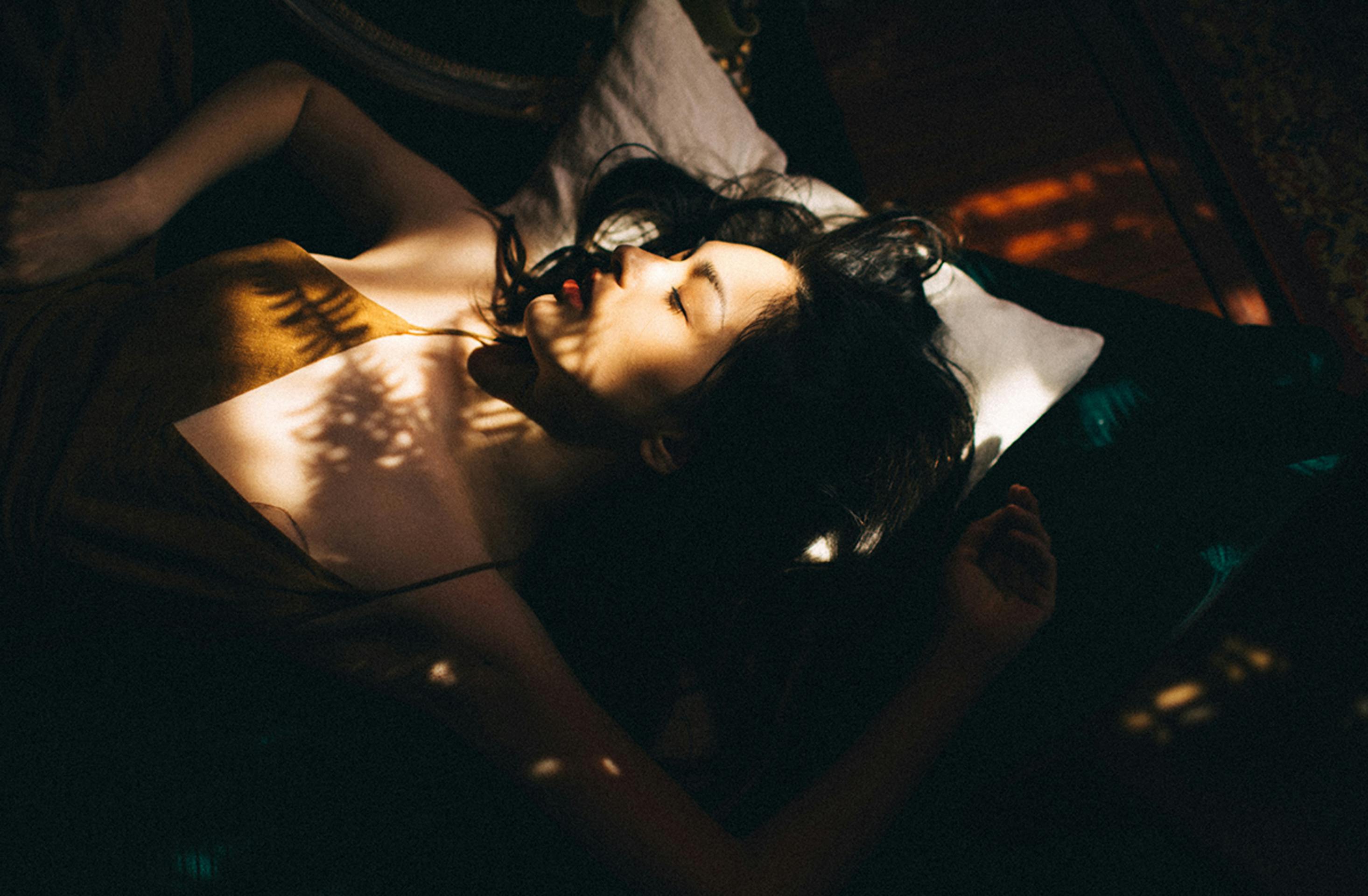 Beautiful woman lying peacefully with sunlight filtering through leaves in a serene setting.