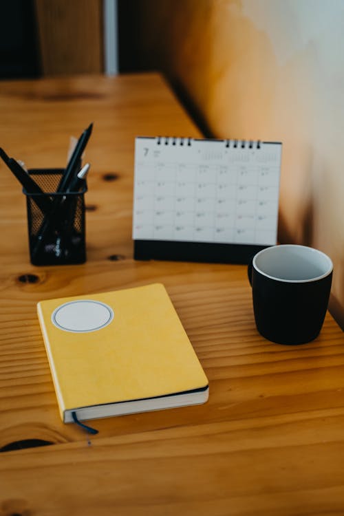 Free Notebook, Calendar and a Black Mug on a Wooden Table Stock Photo
