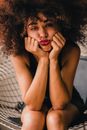 Crop melancholic ethnic female with Afro hair sitting on chair and holding face in hands while looking at camera with sadness