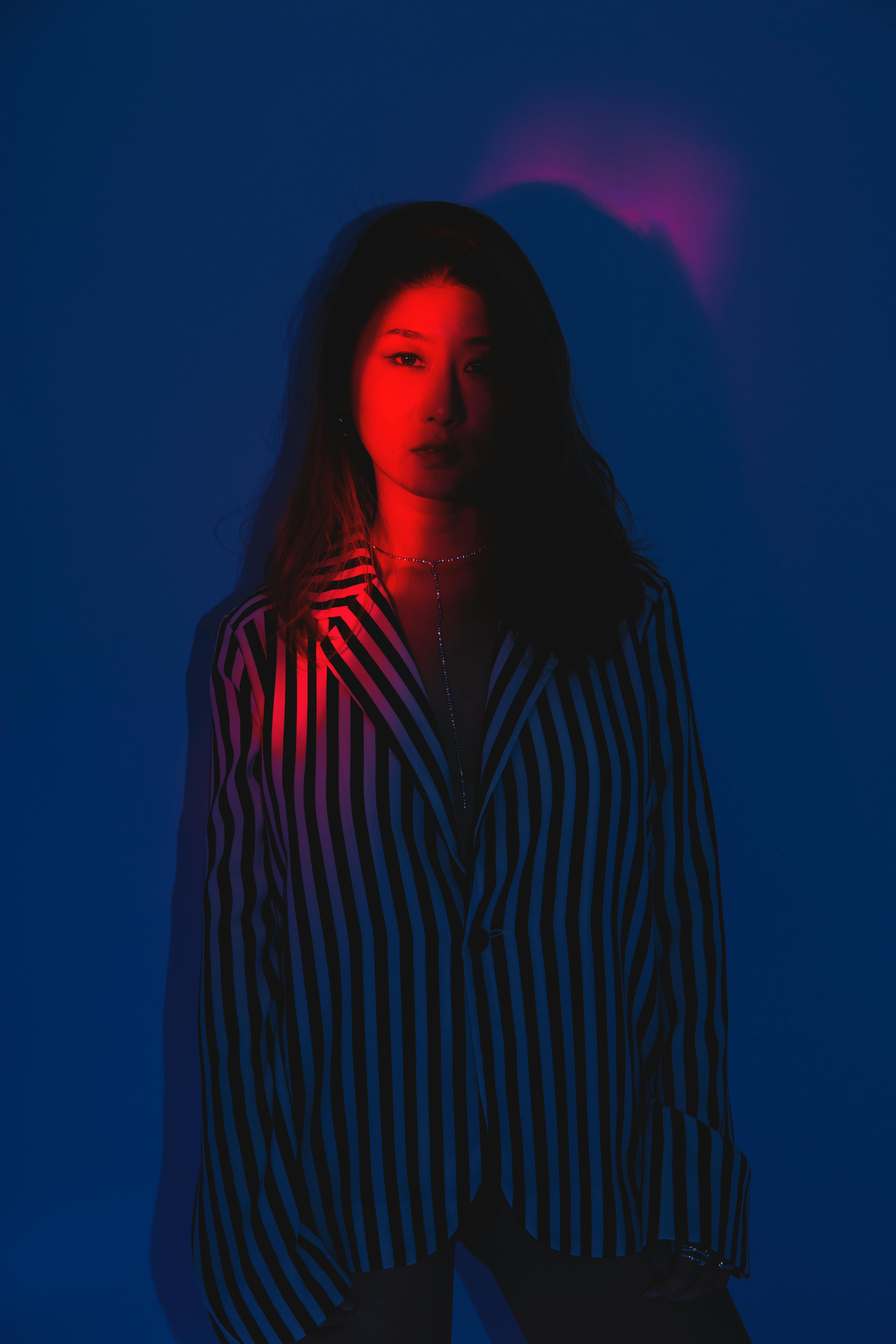 Striking portrait of a stylish woman under dramatic red and blue lighting in a studio setting.
