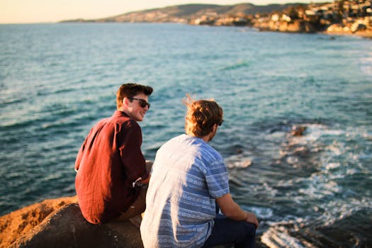 Man Sitting Beside the Seashore Wearing Red Long Sleeve Beside of a Man Wearing White and Grey Polo Shirt