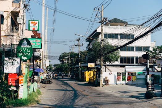A bustling urban street in Chiang Mai, Thailand showcasing shops, power lines, and signages.