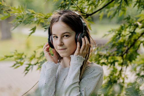 Free A young woman in a gray sweater and headphones enjoying music surrounded by lush greenery. Stock Photo