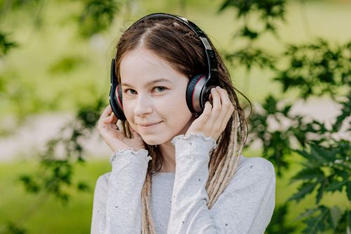 Free A young woman wearing headphones outdoors, enjoying music with a joyful expression. Stock Photo