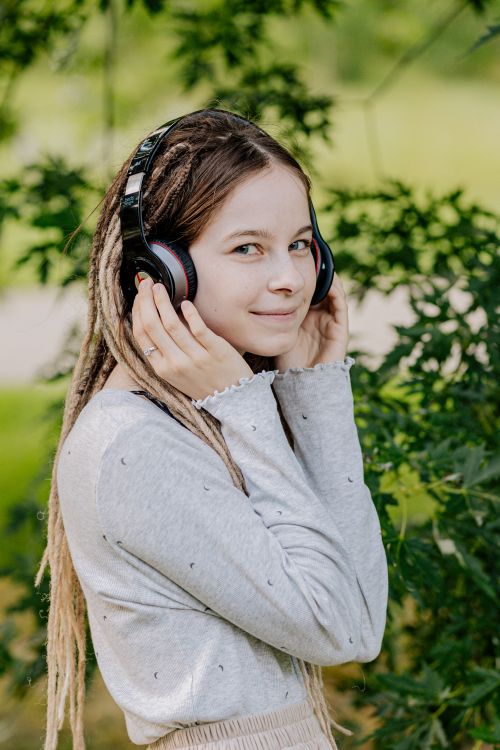 Free Smiling young woman with headphones, listening to music outside in nature. Stock Photo