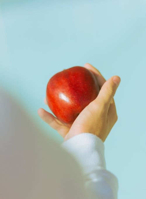 Free A close-up of a hand holding a red apple against a blue background, showcasing freshness and simplicity. Stock Photo
