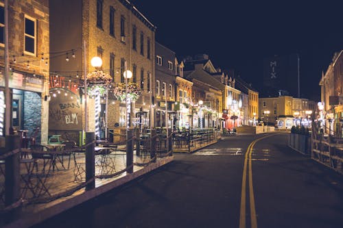 Asphalt roadway between aged building facades and shiny street lamps under dark sky in evening