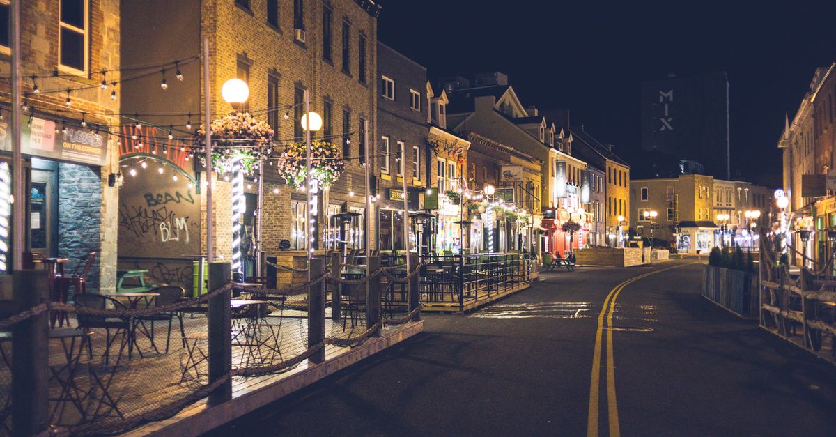 Asphalt roadway between aged building facades and shiny street lamps under dark sky in evening