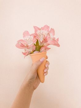 一位匿名女性在米色背景下展示华夫饼上的一束新鲜粉色花朵