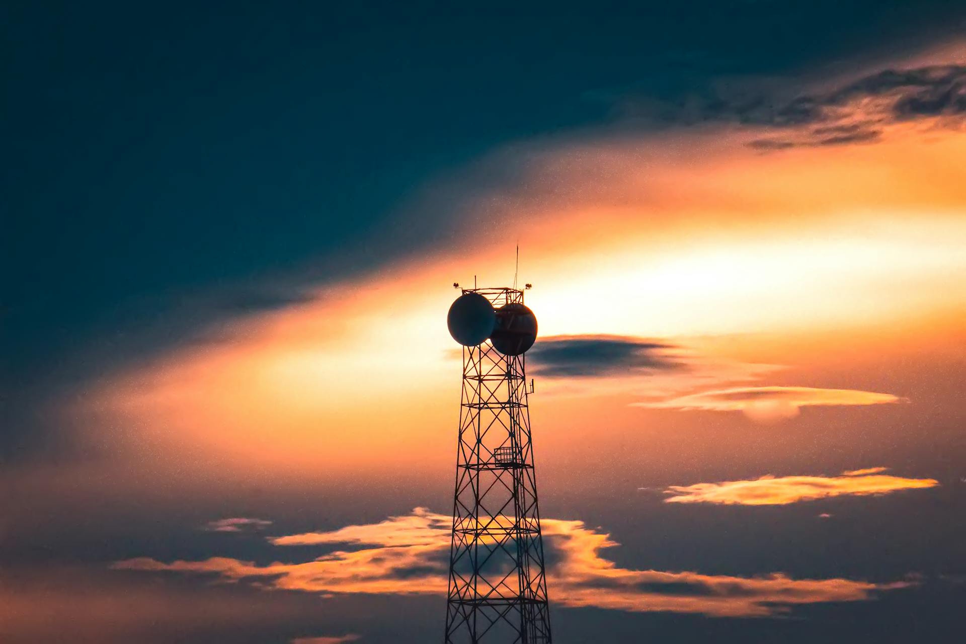 A silhouette of a telecom tower against a dramatic sunset sky in Solapur, India.