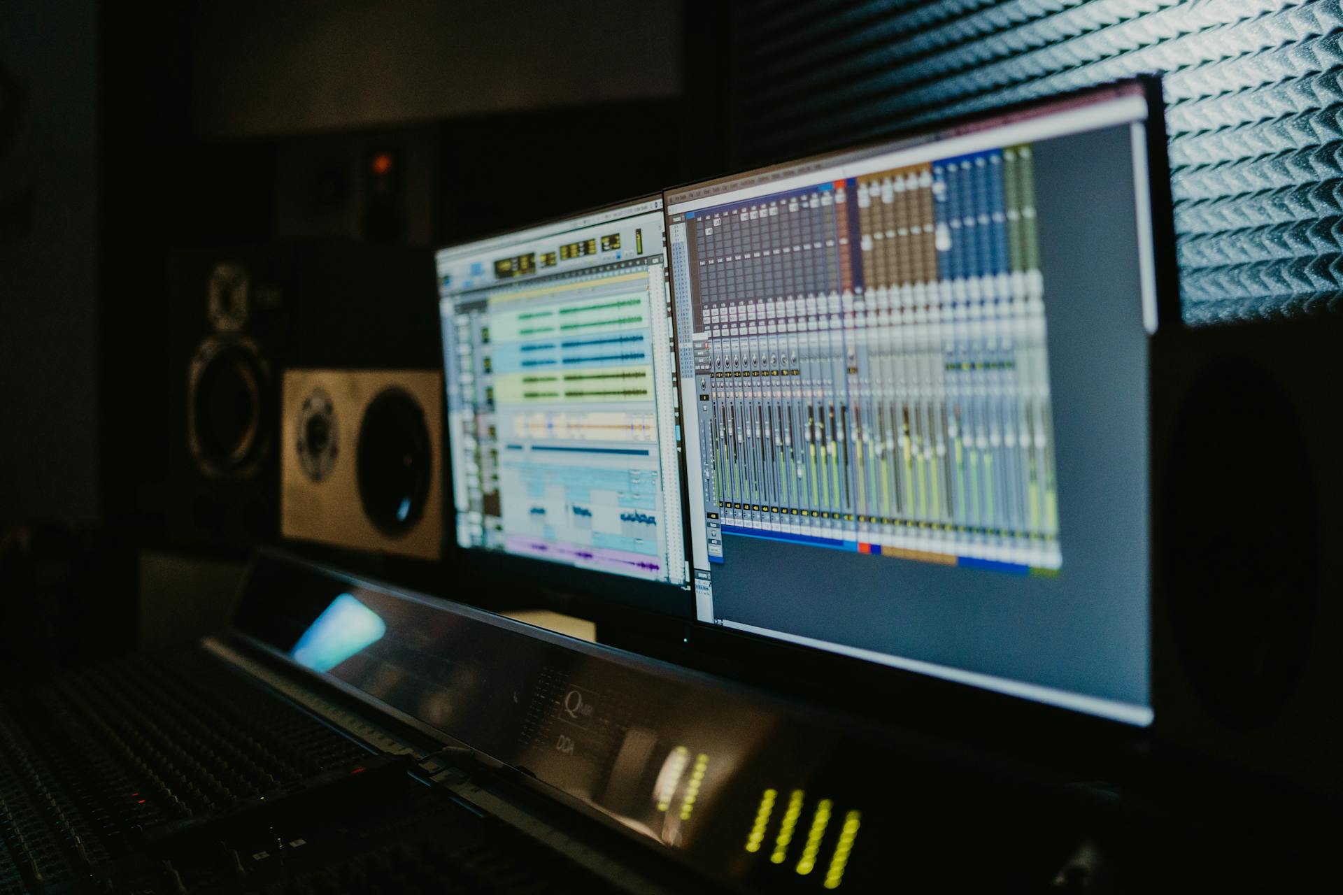 View of a music studio showing dual monitors with audio editing software and professional sound equipment.