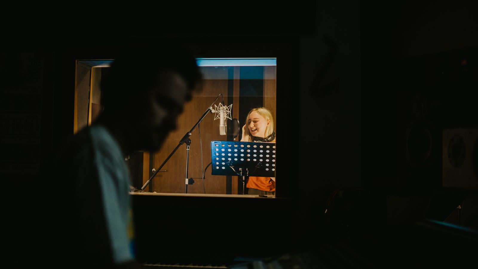 Une chanteuse enregistre sa voix au microphone dans un studio faiblement éclairé.