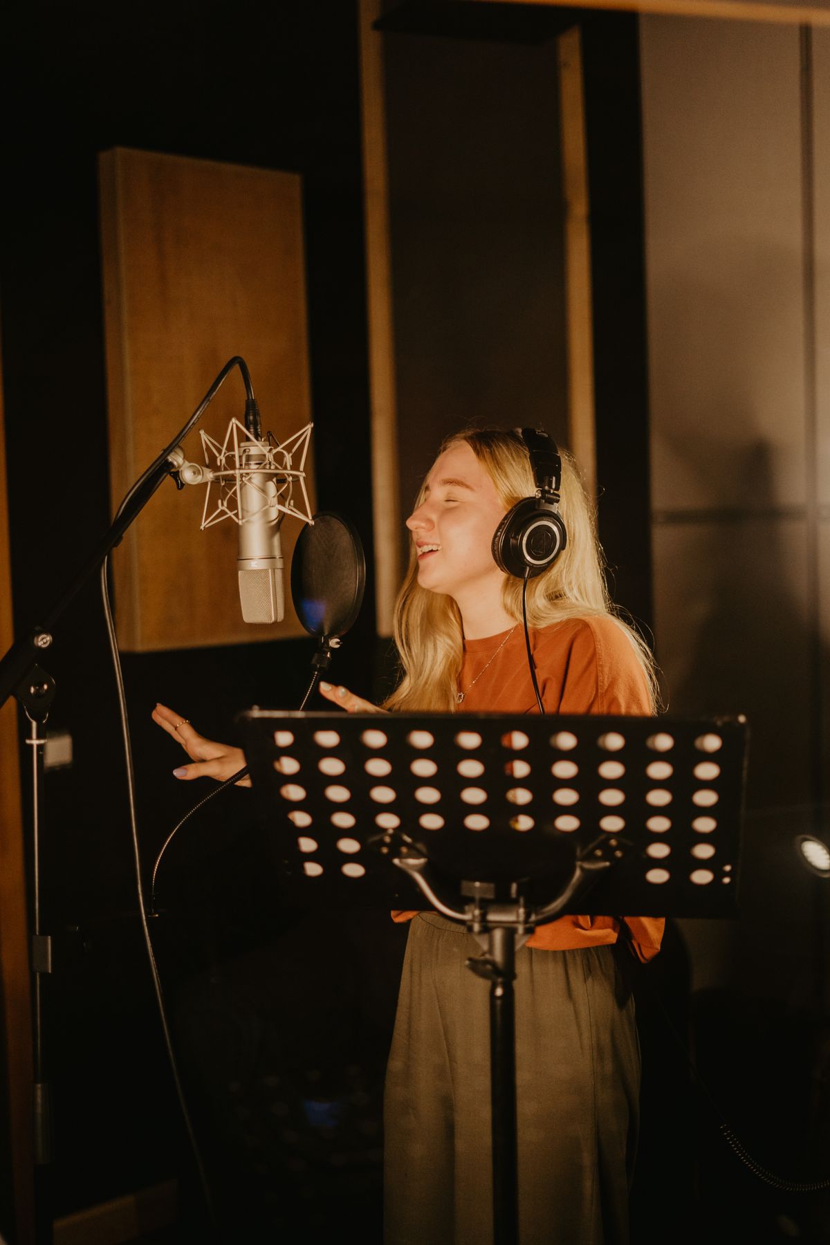 A vocalist recording a custom song in a studio with a microphone and headphones