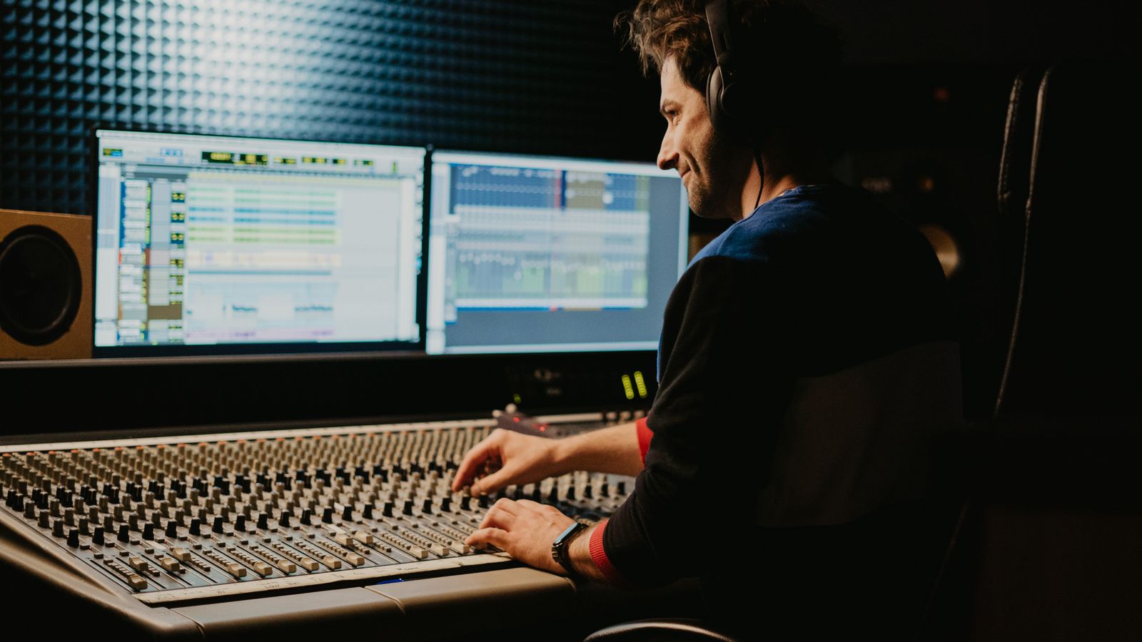 A sound engineer wearing headphones adjusting controls on a mixing console in a recording studio