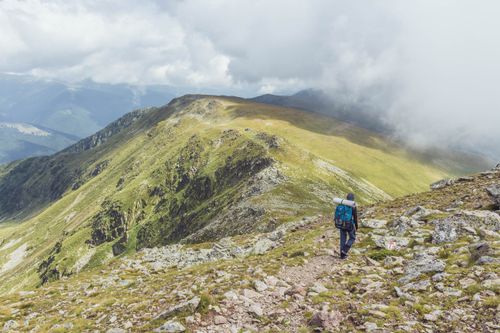Free Full body unrecognizable tourist with big backpack strolling on stony grassy hill range in spectacular highlands on misty day Stock Photo