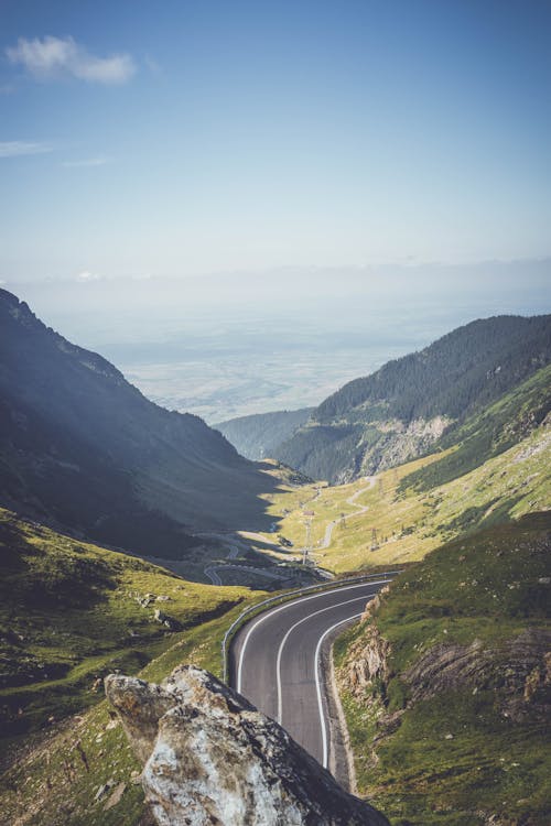 Breathtaking view of empty serpentine roadway surrounded by majestic grassy mountains in sunny picturesque highlands