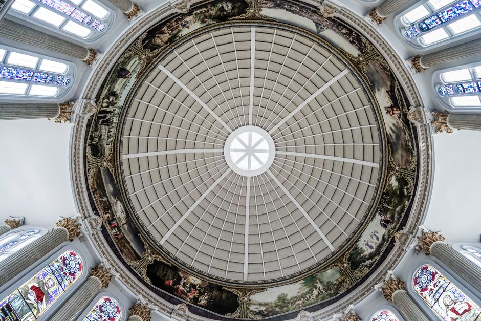 A top-down view of an ornate church ceiling with a painted dome and stained glass windows.