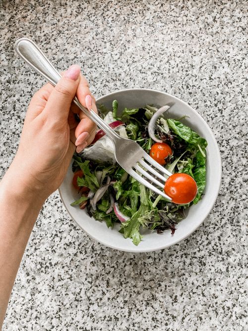Free Top view of unrecognizable female holding fork with cherry tomato above bowl with salad Stock Photo