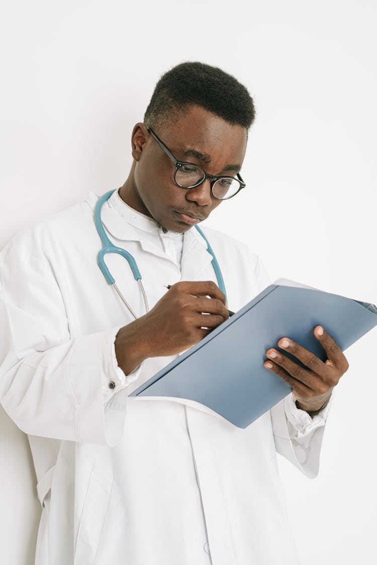 A Doctor Writing On A Folder While Leaning On The Wall