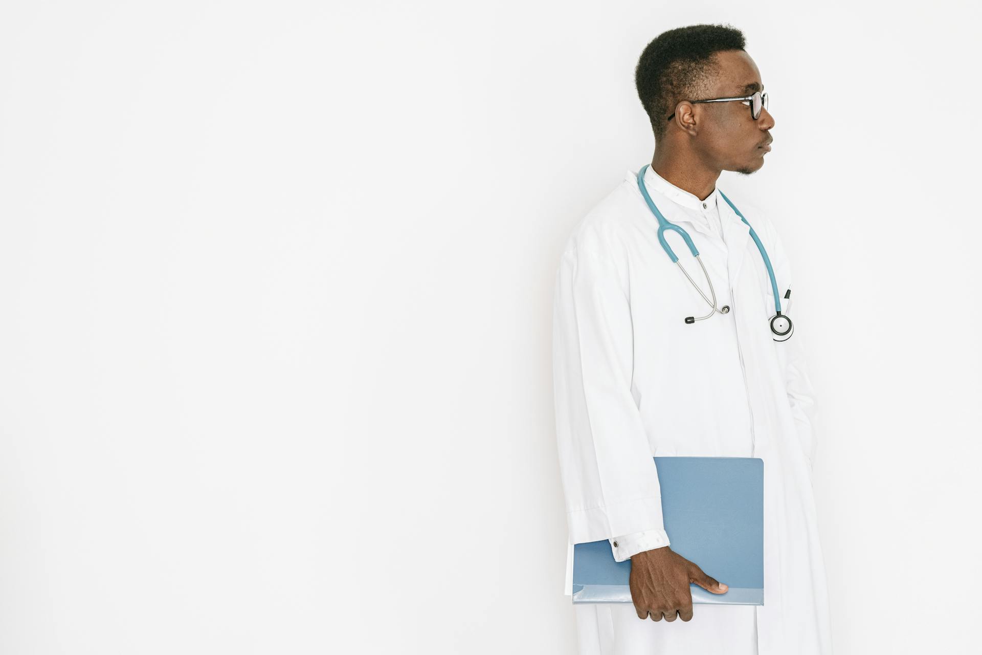 Side profile of a doctor in a medical gown holding a folder with a stethoscope around the neck.