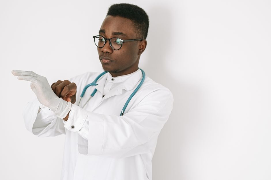 A focused doctor in a medical gown and eyeglasses putting on gloves, symbolizing professionalism. A focused doctor in a medical gown and eyeglasses putting on gloves, symbolizing professionalism.