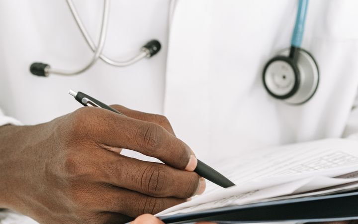 Close-up of a doctor writing on a notepad, wearing a stethoscope around the neck.