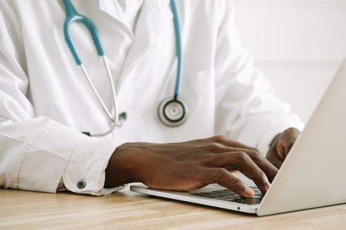 Free Close-up of a doctor using a laptop, wearing a stethoscope and white coat. Stock Photo