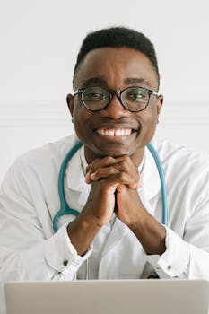 Professional doctor smiling at camera with hands together in workspace.