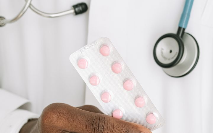A close-up of a doctor holding a blister pack of pills with a stethoscope around their neck.