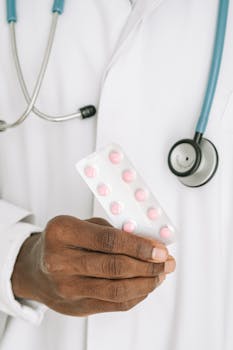A close-up of a doctor holding a blister pack of pills with a stethoscope around their neck.