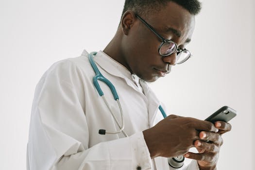 Focused doctor using smartphone, wearing a white coat and stethoscope, indoors.