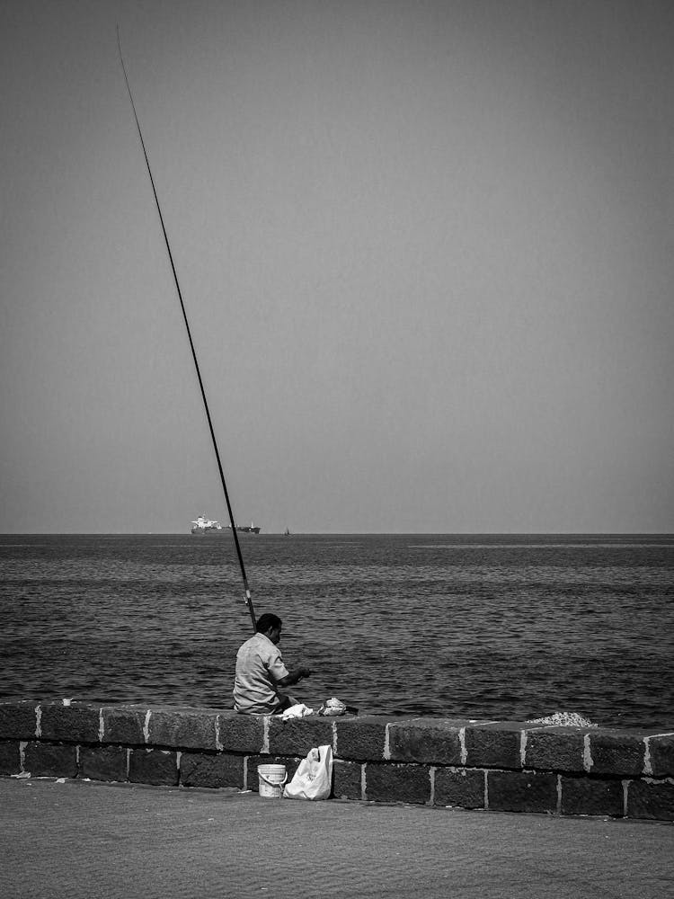 Man Fishing On Brick Pier Of Sea