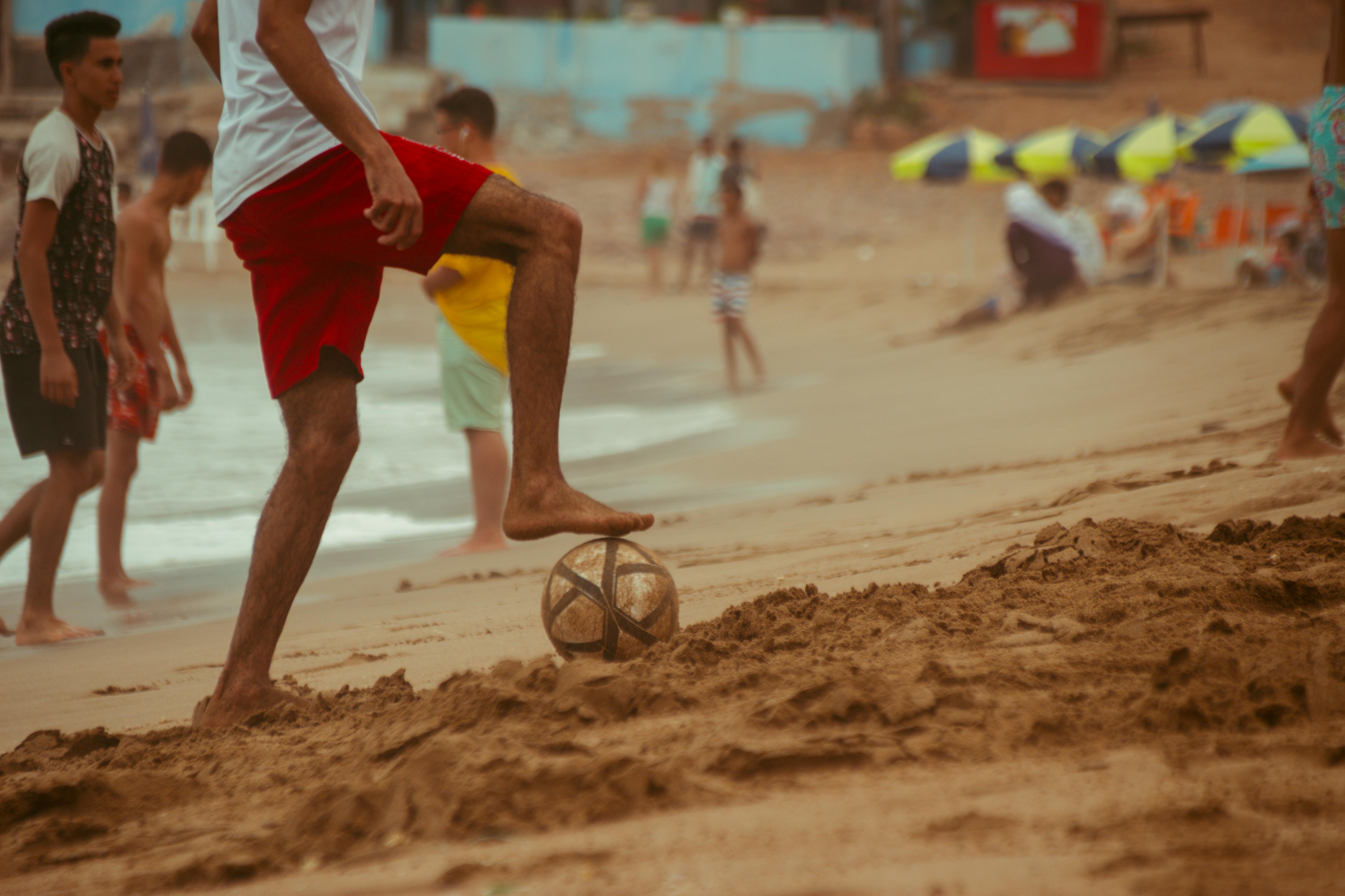 man in red shorts playing soccer at the beach
