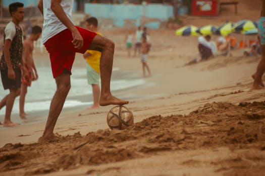 A group of young adults enjoying a game of soccer on a sunny beach, showcasing summer fun.