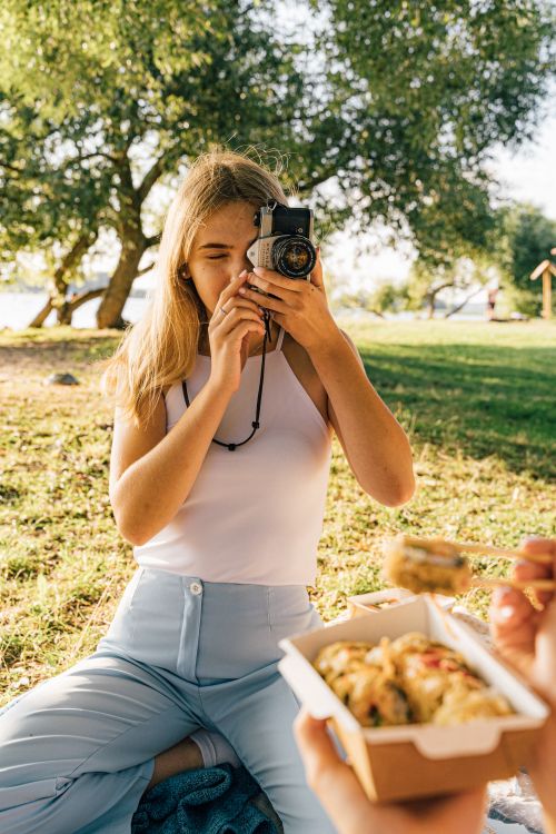 Free Blonde woman photographing with a camera during a picnic in a sunny park. Stock Photo