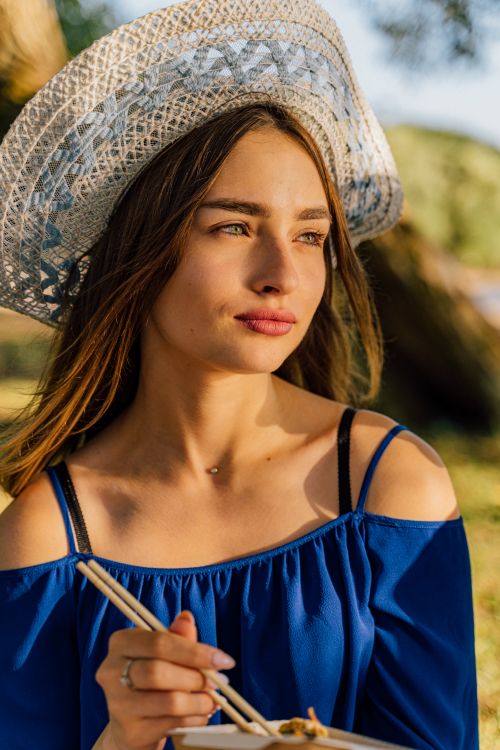Free A young woman in a hat enjoying a meal outdoors in the warm sunlight. Stock Photo