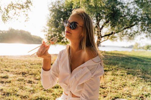 Free Woman in sunglasses enjoys sushi picnic outdoors on a sunny day in the park. Stock Photo