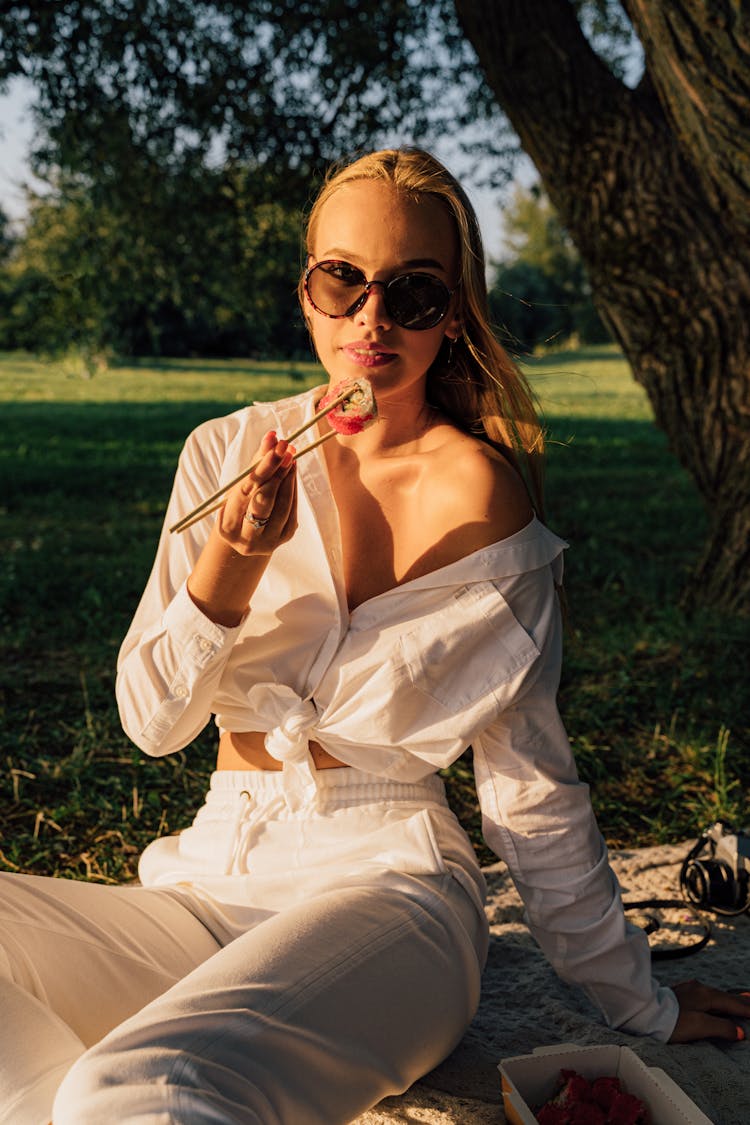A Woman In White Clothing Eating Sushi In The Park