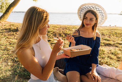 Free Two women enjoying sushi during a relaxing outdoor picnic by the lake. Stock Photo