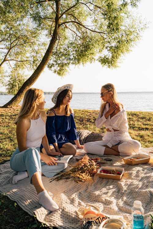 Free Three women enjoying a serene picnic by the lake on a sunny day. Stock Photo